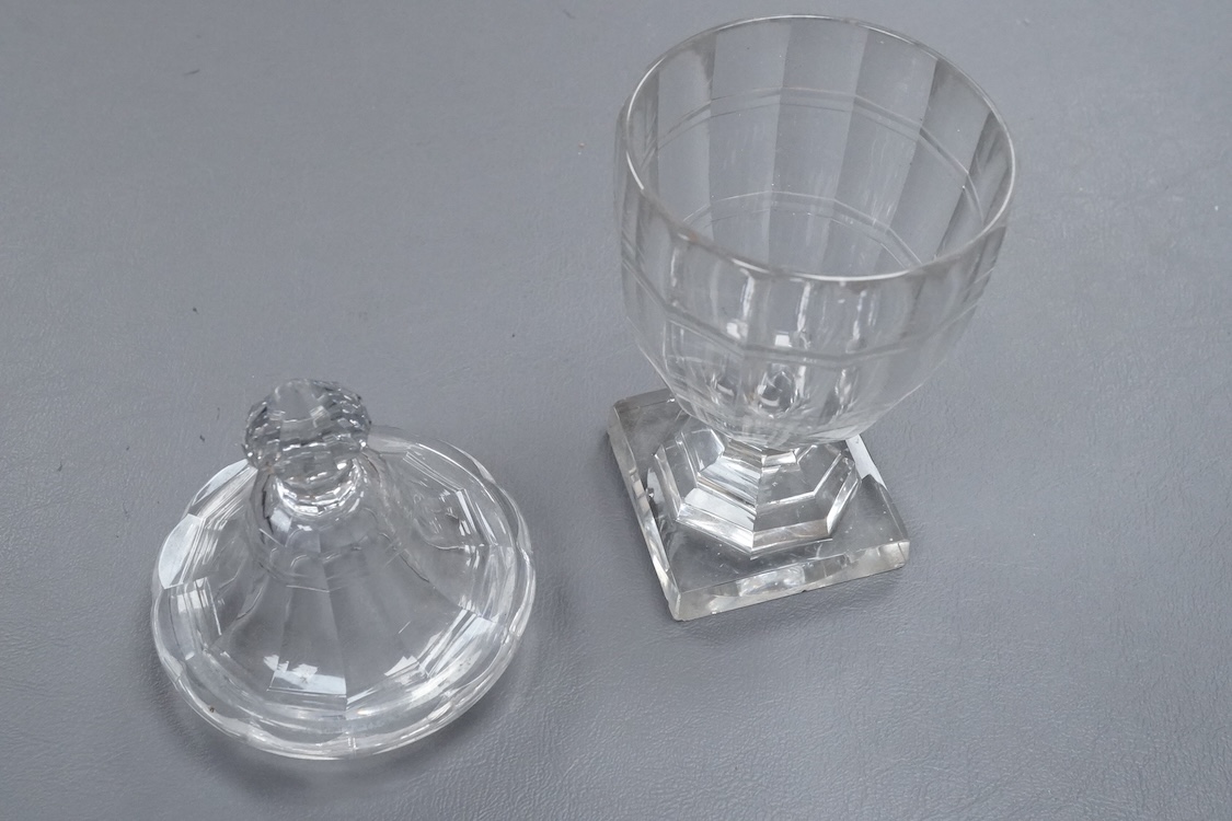 An early 19th century cut glass sweetmeat glass and cover in the shape of an urn, raised on a square pedestal base, with cut out for a spoon to the lid, 21cm high